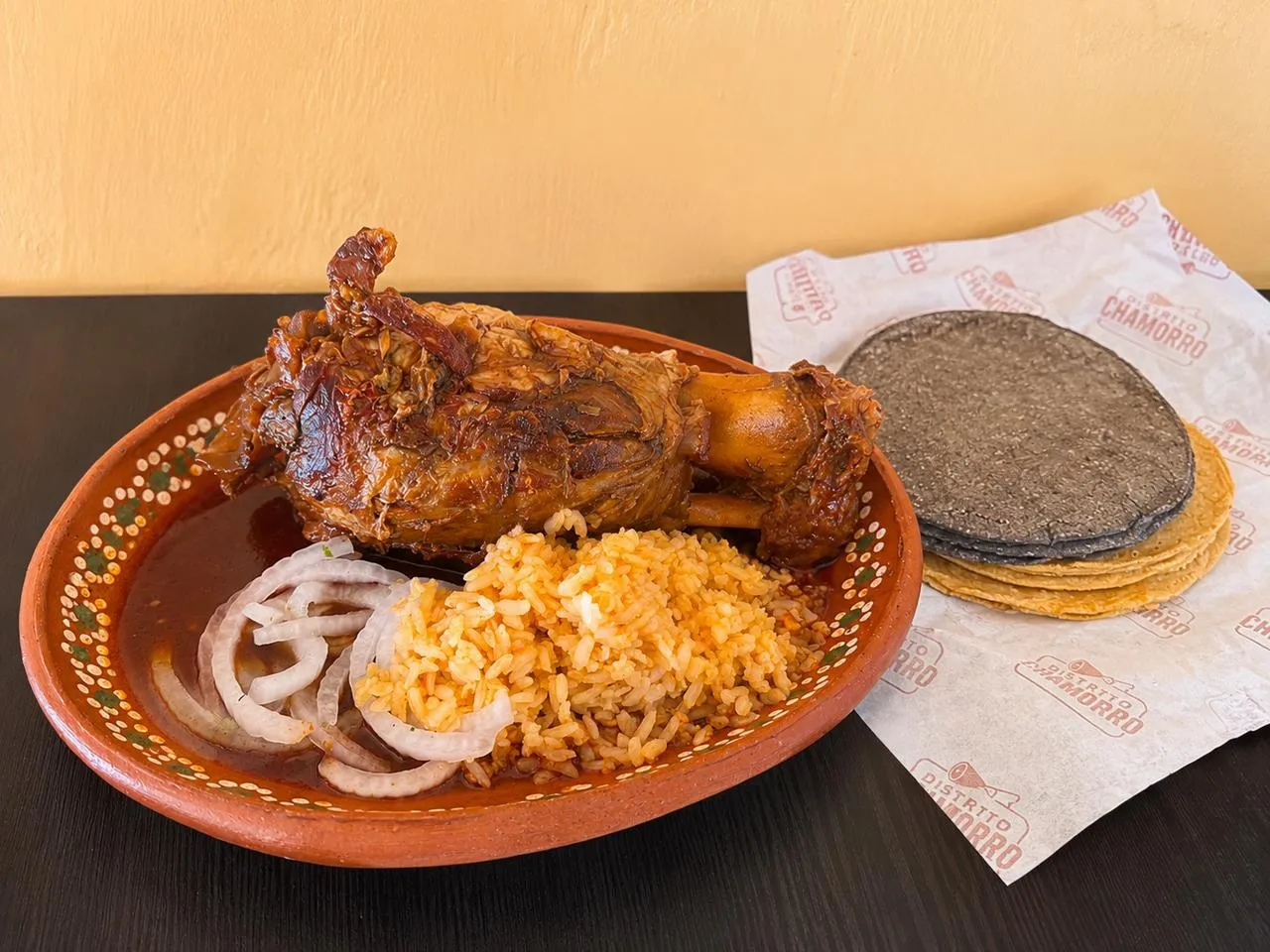 Chamorro entero servido en plato de barro con arroz y cebolla
